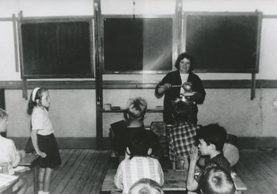 876376 Afbeelding van vrijwilligster Jans Mulder uit Wijk C, die tussen de middag schooleten opschept in een klaslokaal ...